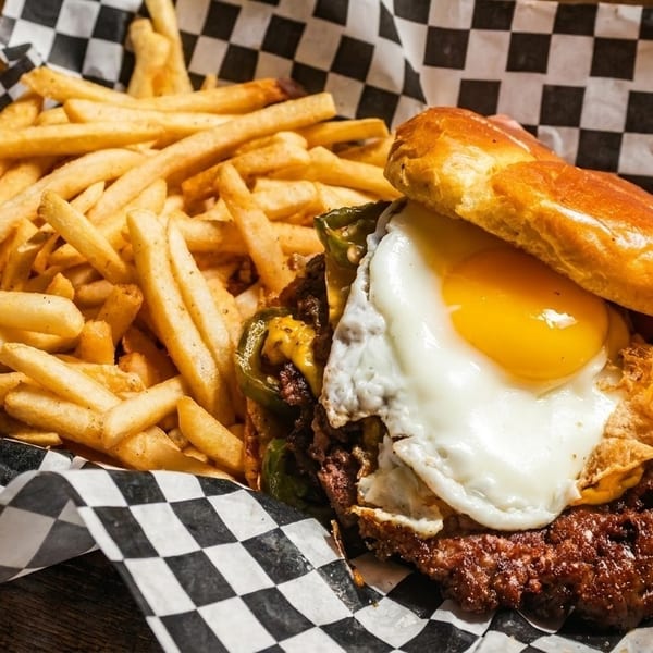 A juicy burger with a fried egg and peppers, served with a side of golden fries.