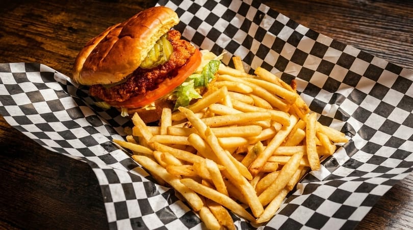 Crispy chicken sandwich with pickles, lettuce, and tomato, served with golden french fries on checkered paper.