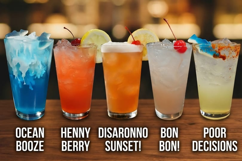 Five colorful cocktails with garnishes, including a blue drink with gummy sharks, on a wooden bar.