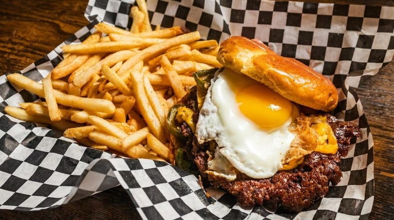 A burger with a fried egg and peppers, served with a side of french fries.