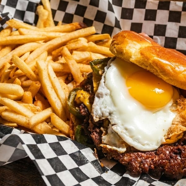 A burger with a fried egg and jalapeños, served with a side of golden french fries.